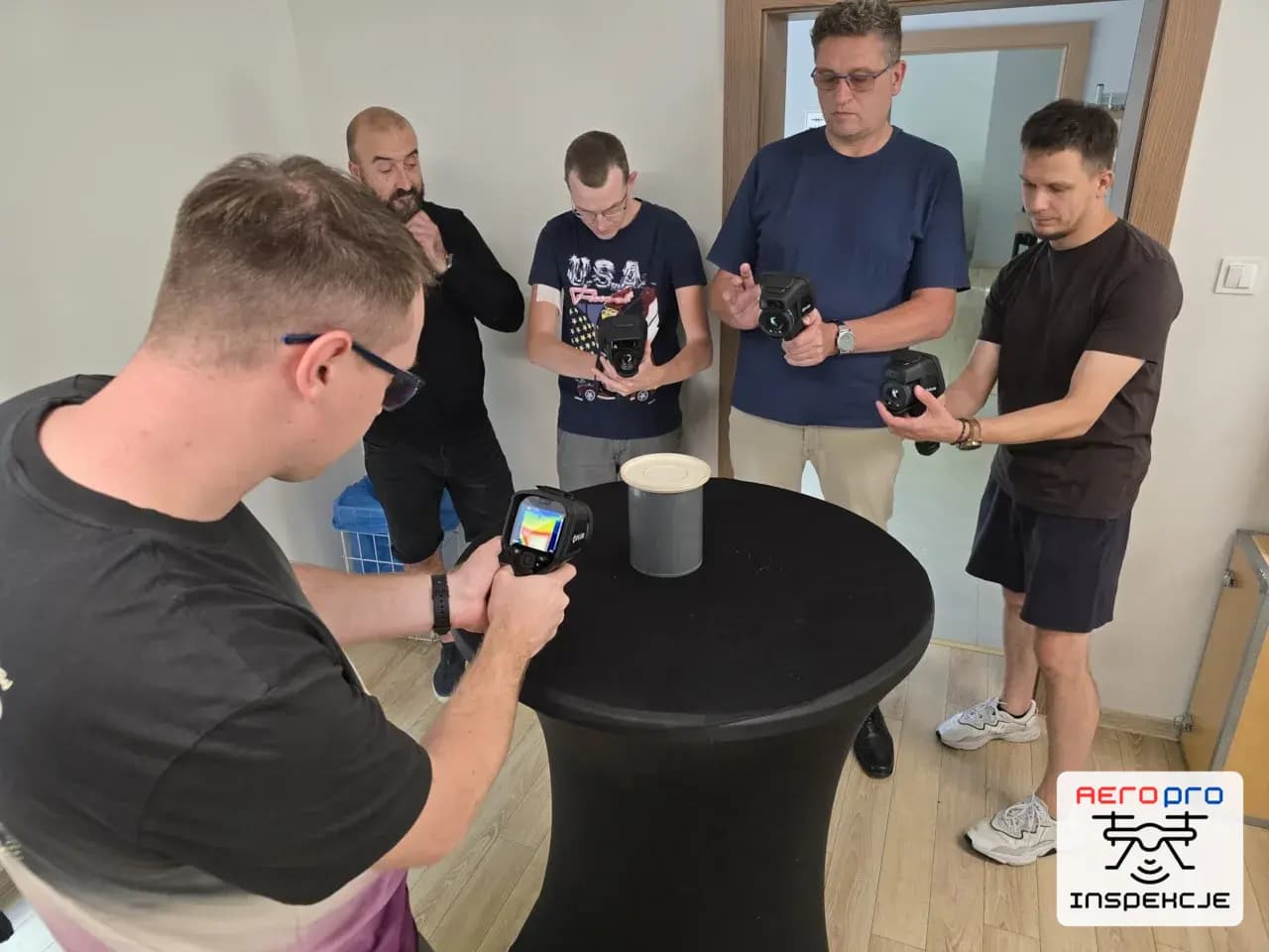 Uczestnicy szkolenia ćwiczący obsługę kamery termowizyjnej przy stoliku